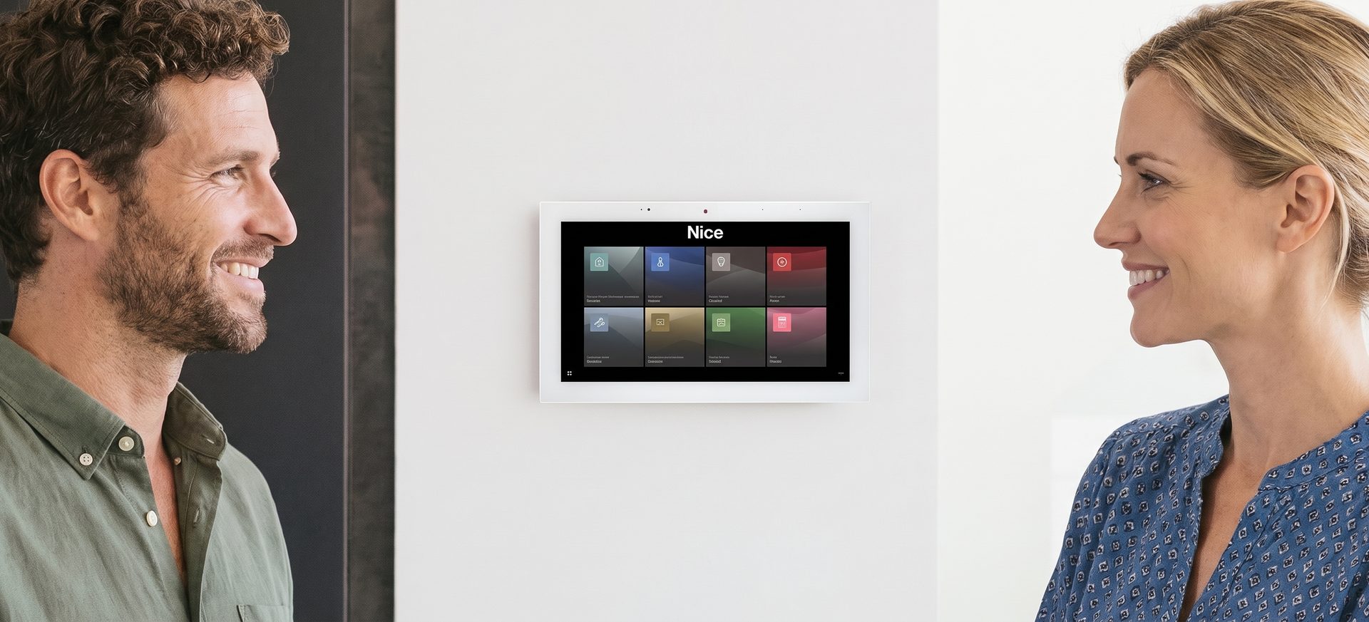 Two people smiling beside an ELAN touch panel on the wall