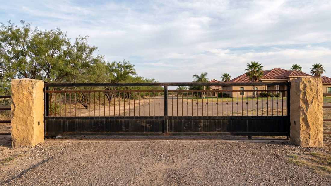 A steel driveway gate between stone pillars at a South Texas property