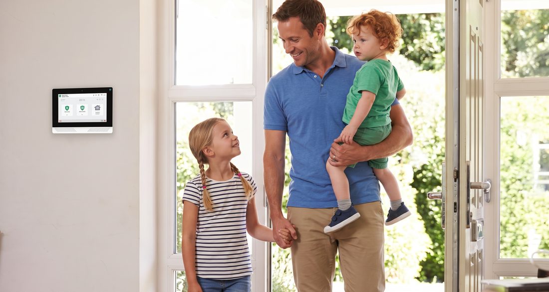 A father and two children coming home, with a security panel on the wall